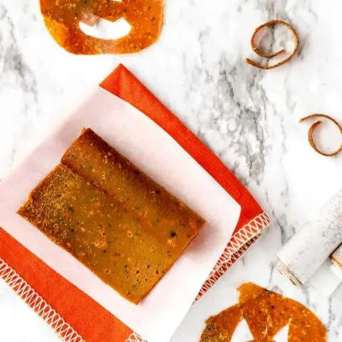 Rolled up pumpkin fruit leather on parchment paper and orange napkin