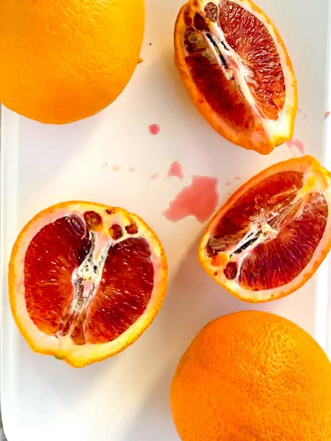 Blood oranges sliced open on white plate with orange juice 