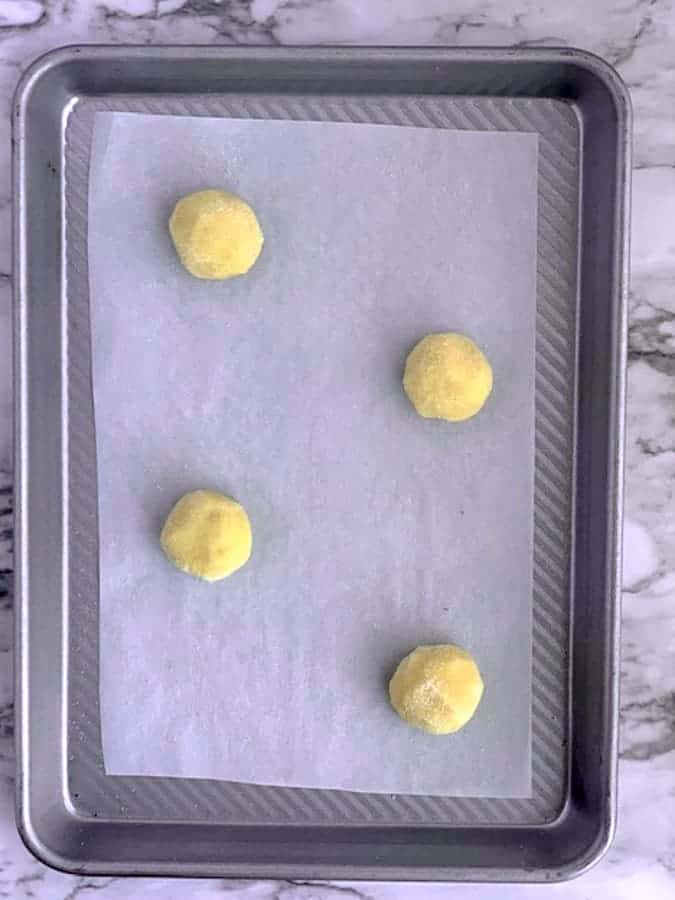 Four balls of almond flour sugar cookie dough on a parchment lined baking sheet