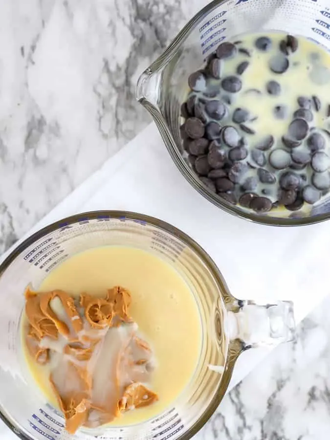 Sweetened condensed milk and chocolate chips and peanut butter in glass measuring cups