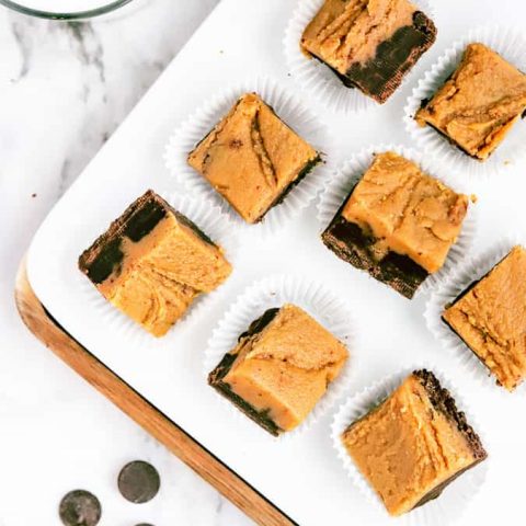 Squares of chocolate peanut butter fudge on a white plate and marble countertop