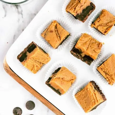 Squares of chocolate peanut butter fudge on a white plate and marble countertop