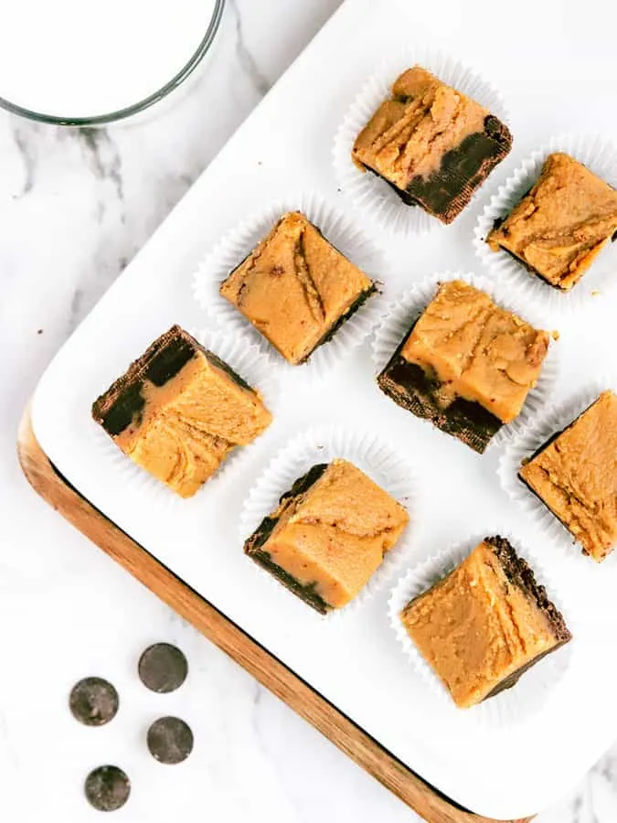 Squares of chocolate peanut butter fudge on a white plate and marble countertop