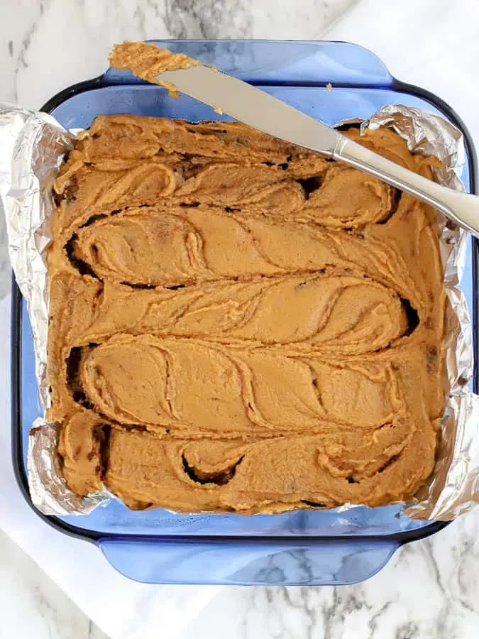 Swirls of peanut butter and chocolate fudge in a blue pan with knife resting on side