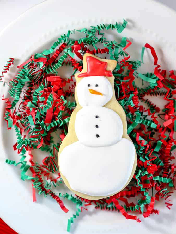 Snowman cookie decorated with royal icing on white plate with red and green confetti