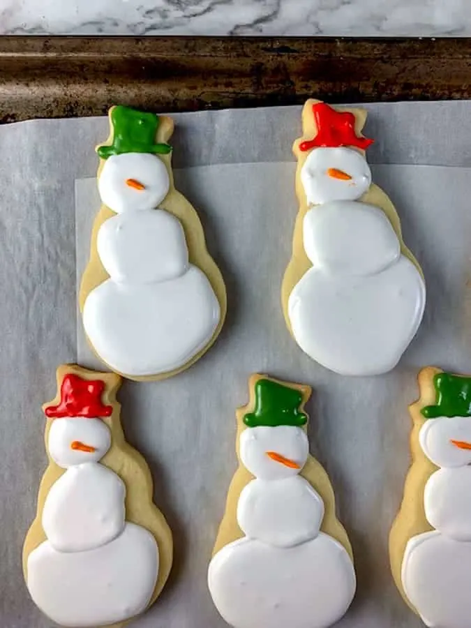 Snowman cut out cookies decorated with royal icing and red and green hats
