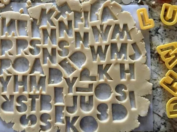 sugar cookie dough rolled out with letter cookie cutters and letters in dough