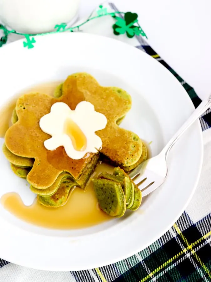 Shamrock shaped spinach pancakes on a plate with butter and syrup