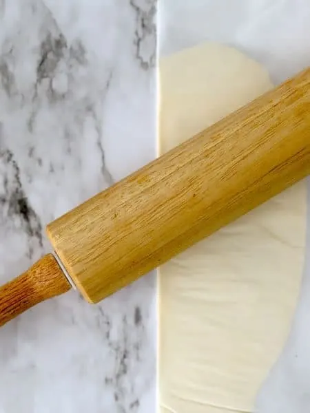 Rolling pin flattens out pats of butter between parchment paper