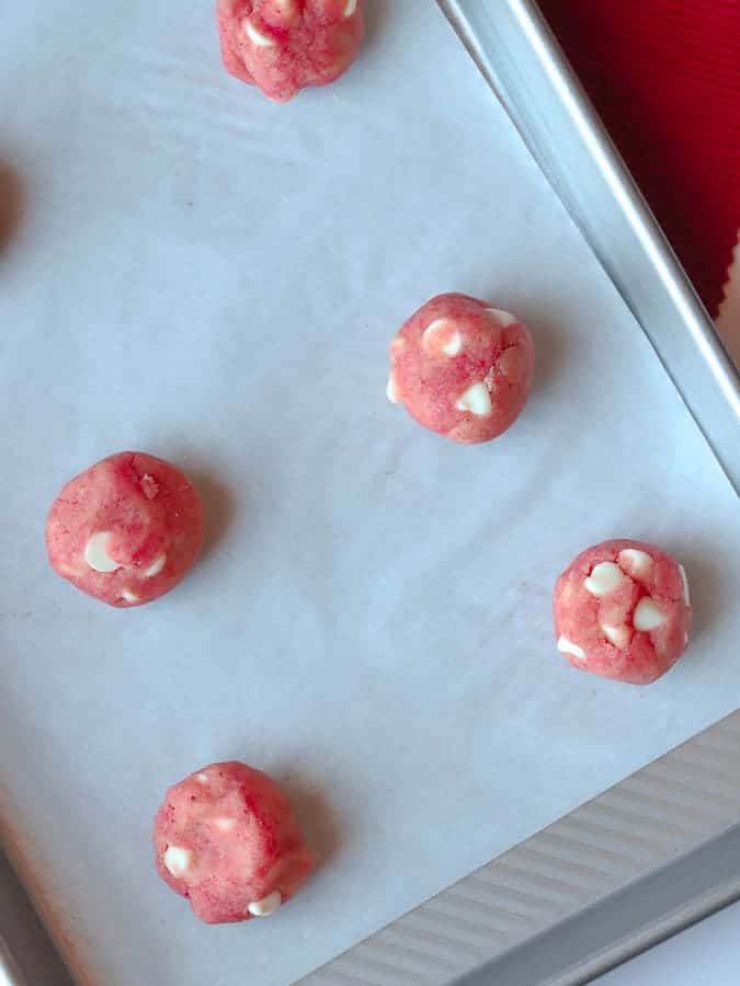 Rounds of pink cookie dough with white chocolate chips on baking tray
