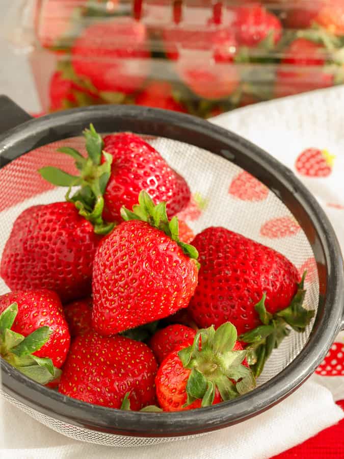 Fresh organic strawberries in a strainer on to of strawberry towel