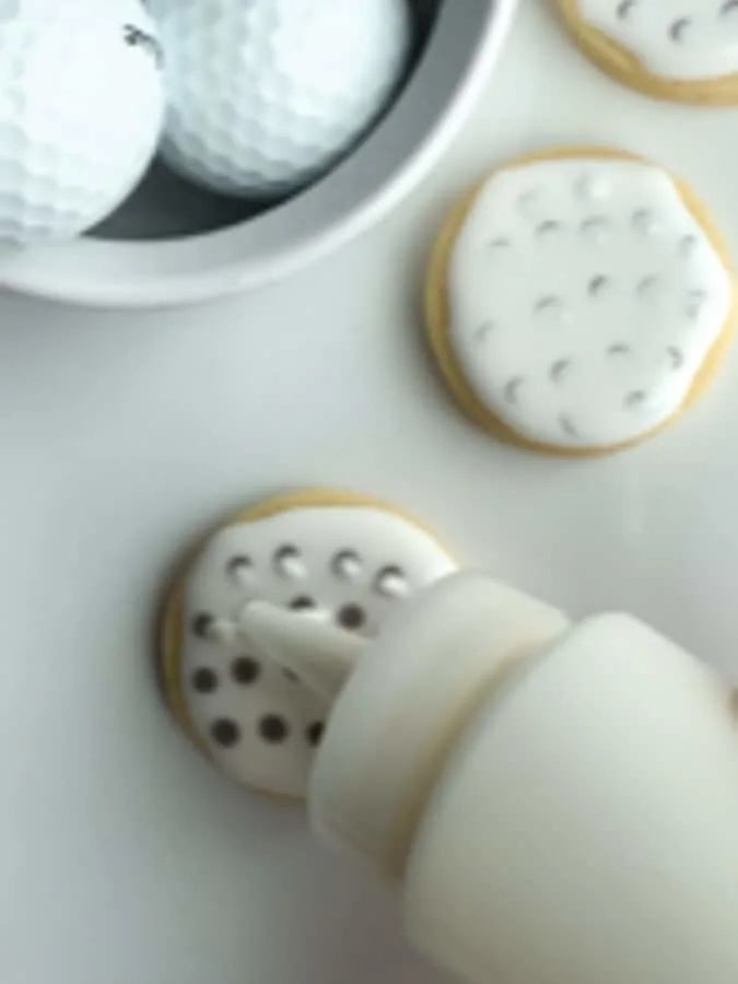 add white royal icing circles on top of the gray royal icing to make dimples for golf ball cookies
