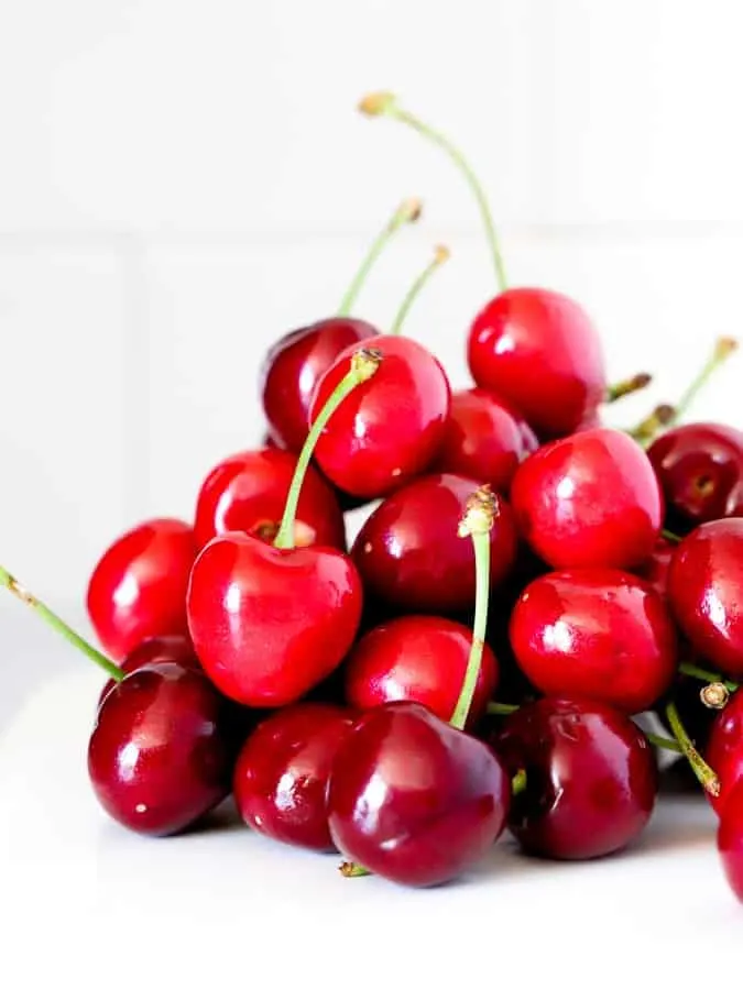 Fresh cherries in a pile on a white plate and white tile background