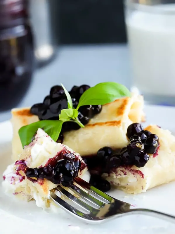 Two blueberry blintz with Greek yogurt filling on a white plate with fork