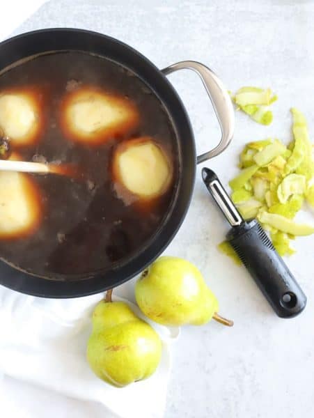 Pears in poaching liquid with peeler on board