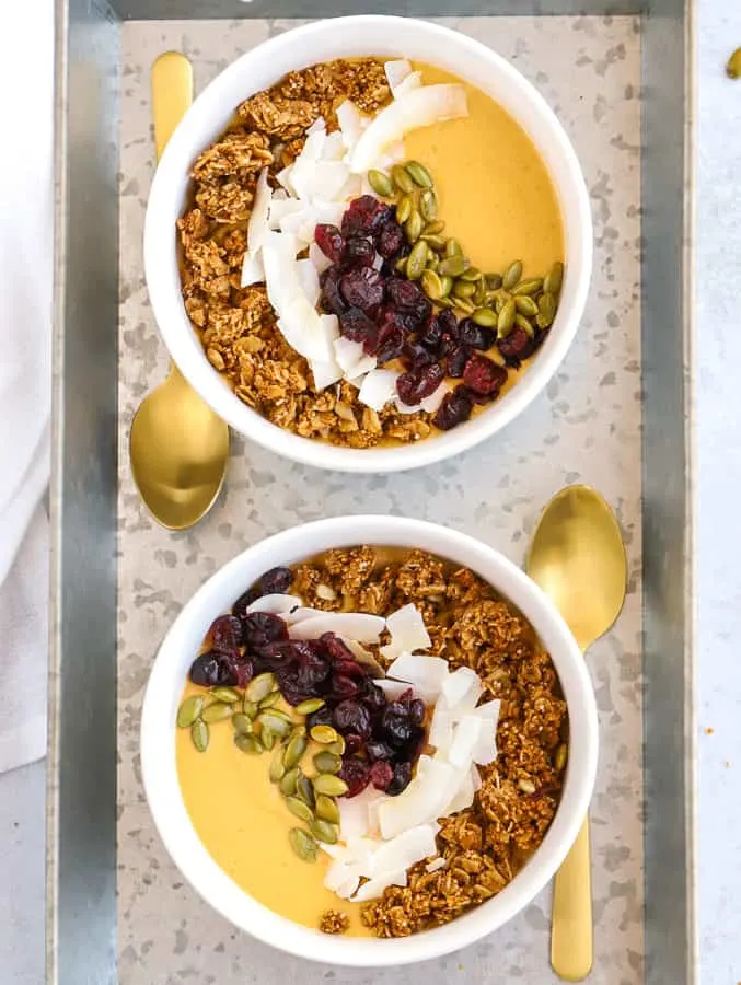 two bowls of pumpkin smoothie with granola, coconut chips, and pepitas