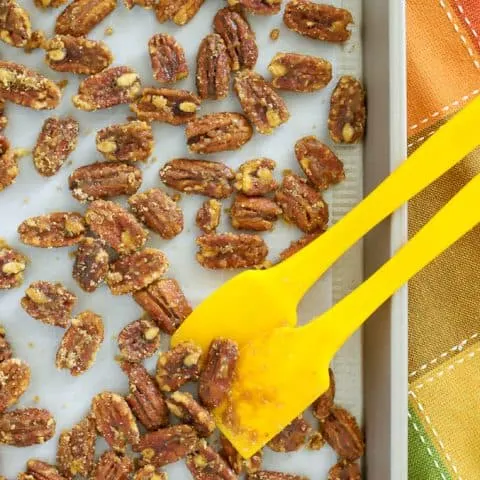 Candied pecans spread on parchment lined baking sheet with two yellow spatulas