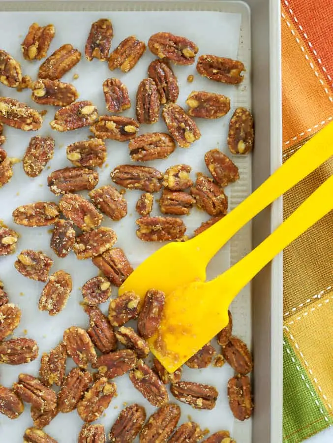Candied pecans spread on parchment lined baking sheet with two yellow spatulas