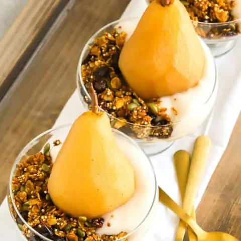 Poached pears with non dairy yogurt, granola for breakfast on wooden tray with gold spoons