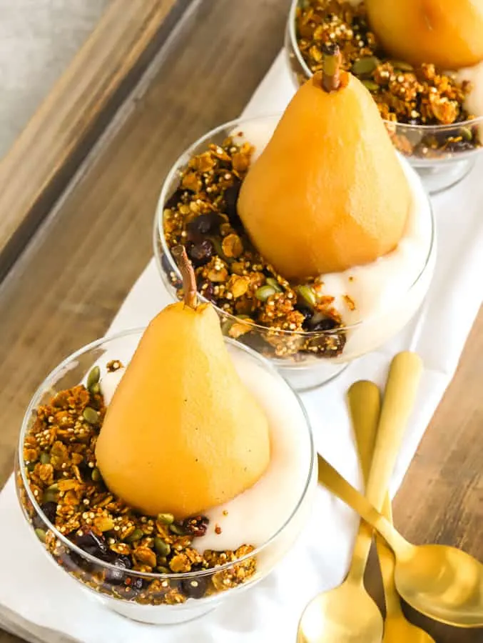 Poached pears with non dairy yogurt, granola for breakfast on wooden tray with gold spoons