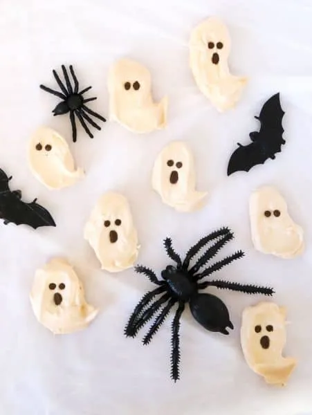 Ghost meringues with chocolate faces and pretend black spiders on a white background