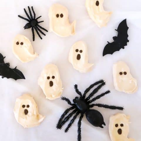 Ghost meringues with chocolate faces and pretend black spiders on a white background