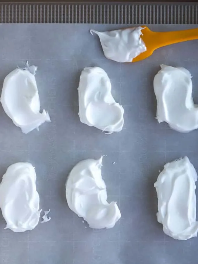 ghost meringues on a baking sheet with yellow spatula