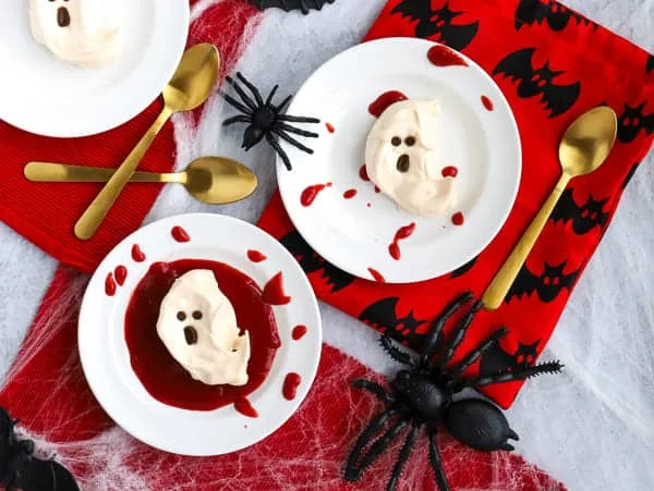 two white plates with ghost meringues with strawberry sauce and splatters