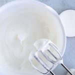 egg whites in white bowl whipped to soft peaks with electric mixer