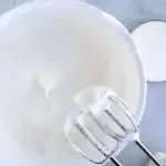 egg whites in white bowl whipped to soft peaks with electric mixer