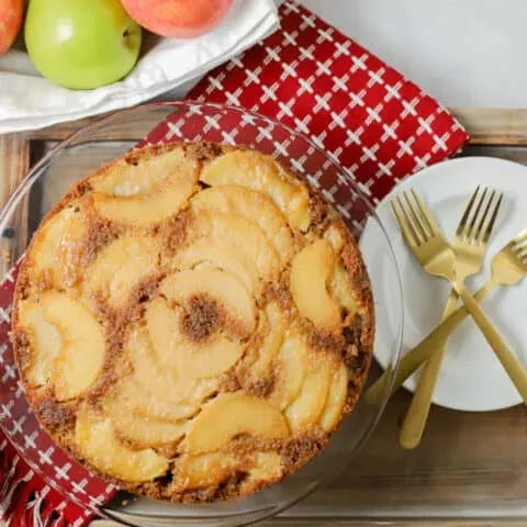 Upside down apple cake on a red kitchen towel with white plates and gold forks