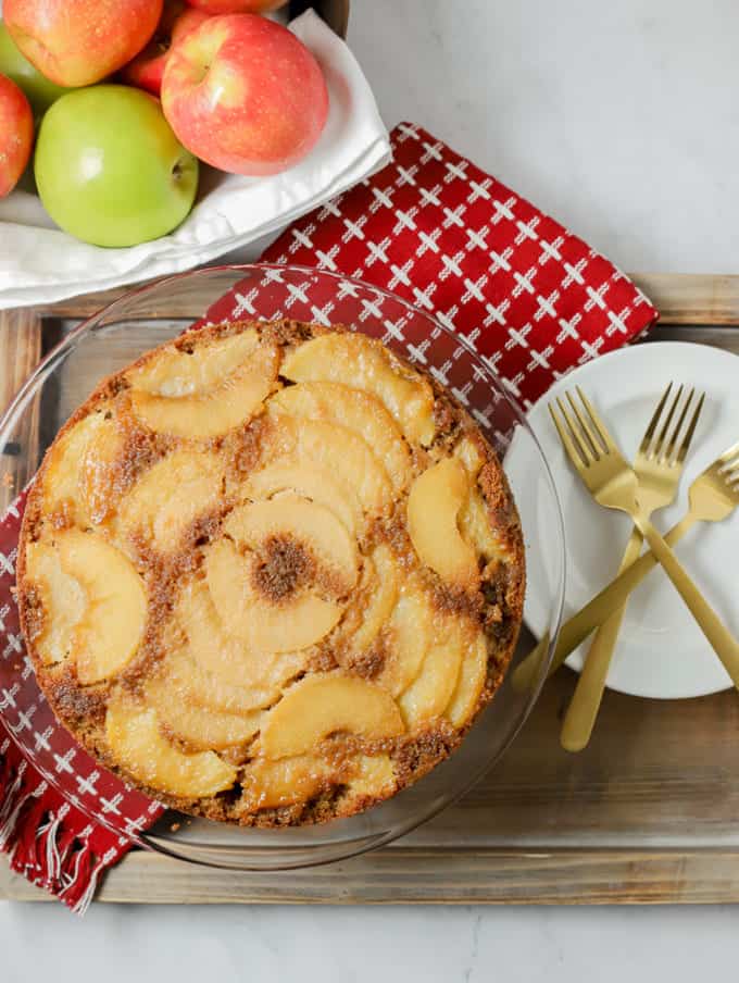 Upside down apple cake on a red kitchen towel with white plates and gold forks