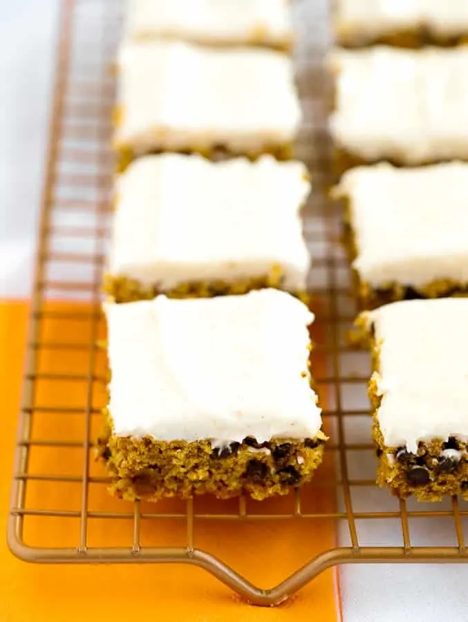 Gluten free pumpkin bars with cream cheese frosting on gold wire baking rack 