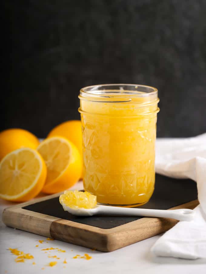 lemon curd in ball canning jar with white spoon and sliced lemons