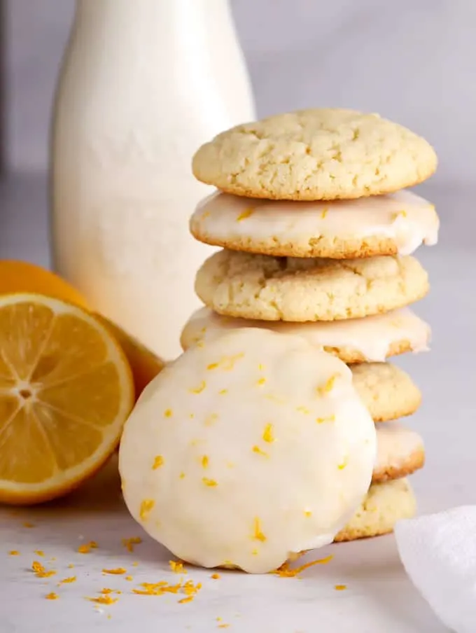 tall stack of lemon cookies with lemon icing glaze and a bottle of milk and a lemon