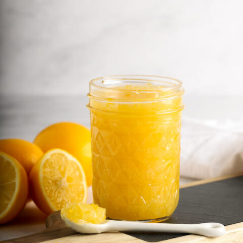 Jar of vegan lemon curd on black and wooden cutting board with sliced lemons