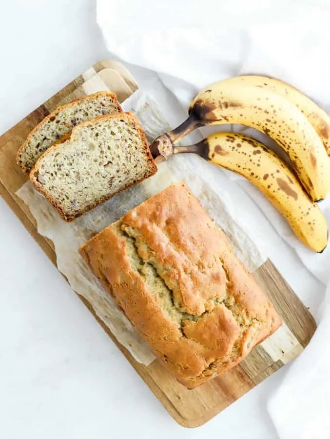 Moist banana bread sliced on cutting board with 3 bananas