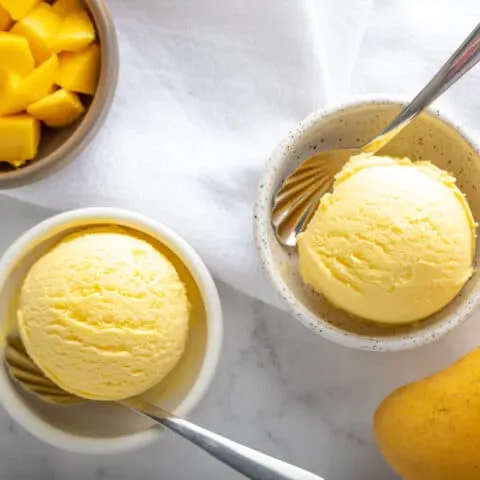 two scoops of mango gelato in two bowls with diced mango