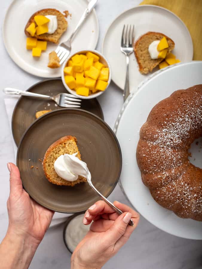 Slice of mango cake with dollop of yogurt and bundt cake in background