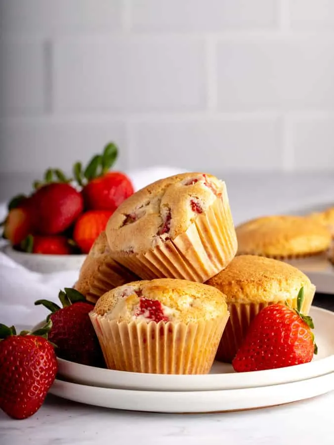 group of four strawberry muffins on white plates with fresh strawberries