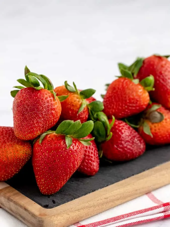 Fresh strawberries on a slate and wooden board with white and red towel underneath