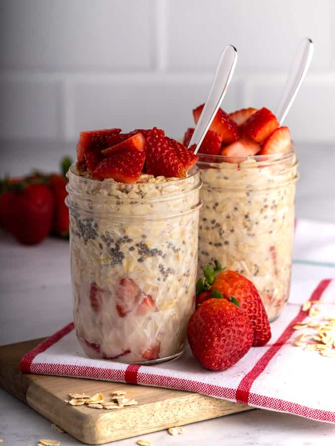 two mason jars of overnight oats breakfast with strawberries on wooden cutting board