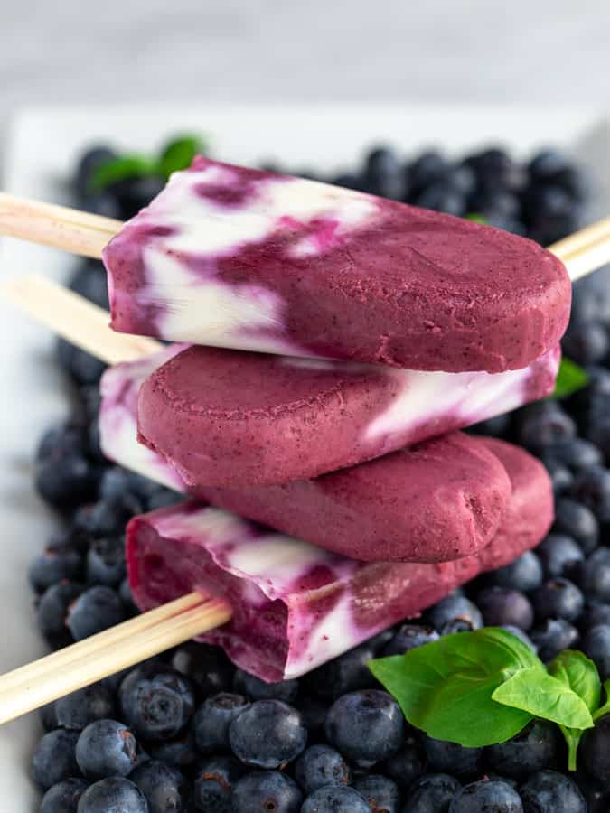 Four blueberry creamsicle popsicles stacked up with fresh blueberries 