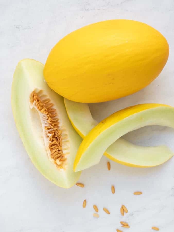 Whole yellow canary melon with slices of melon and seeds on marble surface