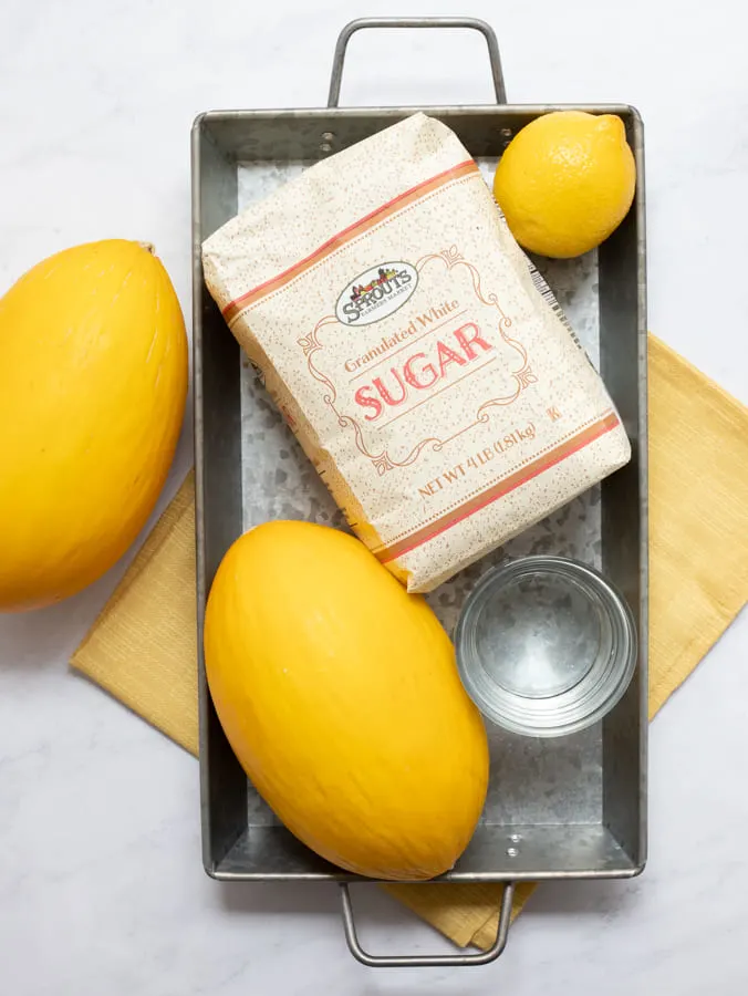 Sprouts Granulated Sugar Bag, Two Yellow Canary Melons, one lemon and water on silver tray