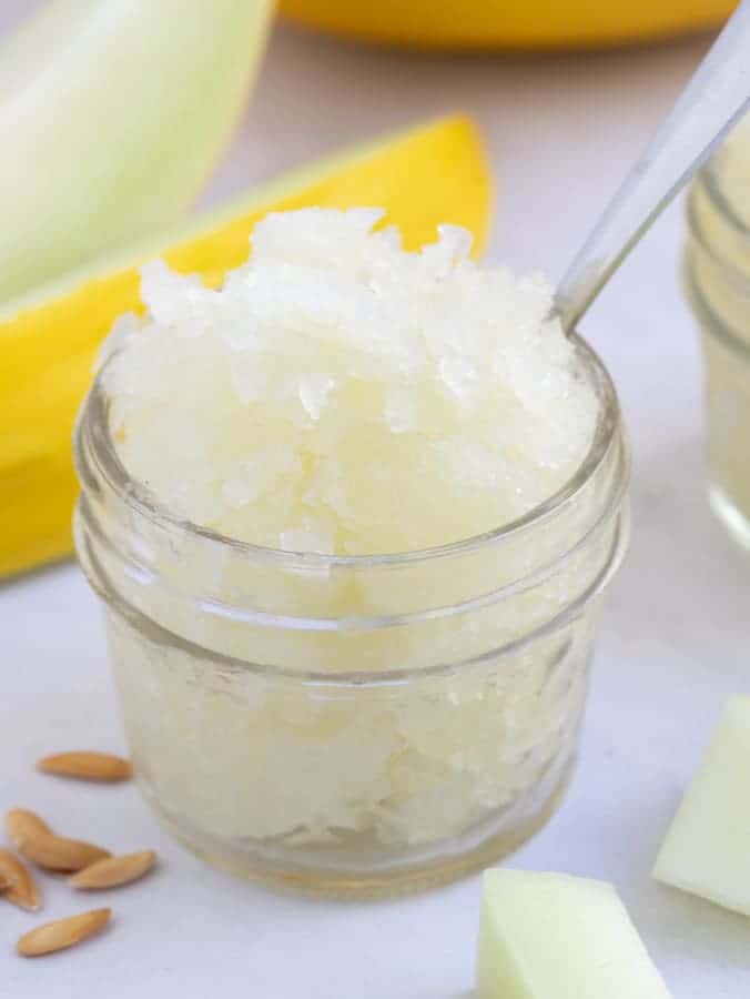 Close up single small glass jar filled with melon granita and silver spoon