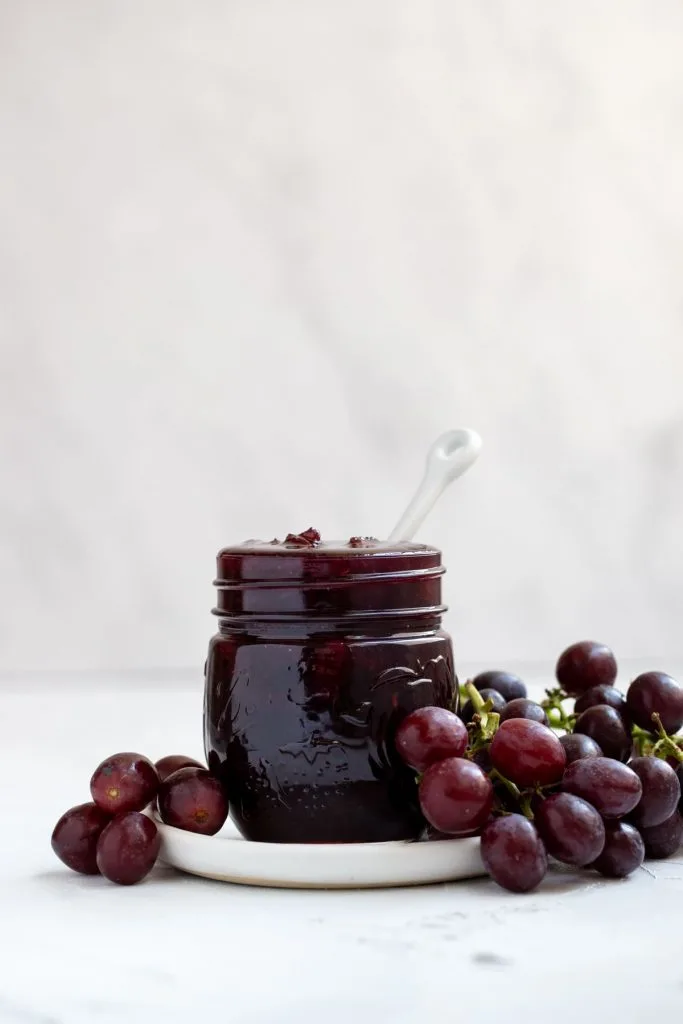 Homemade grape jam filled to the top of mason jar with fresh grapes on the side