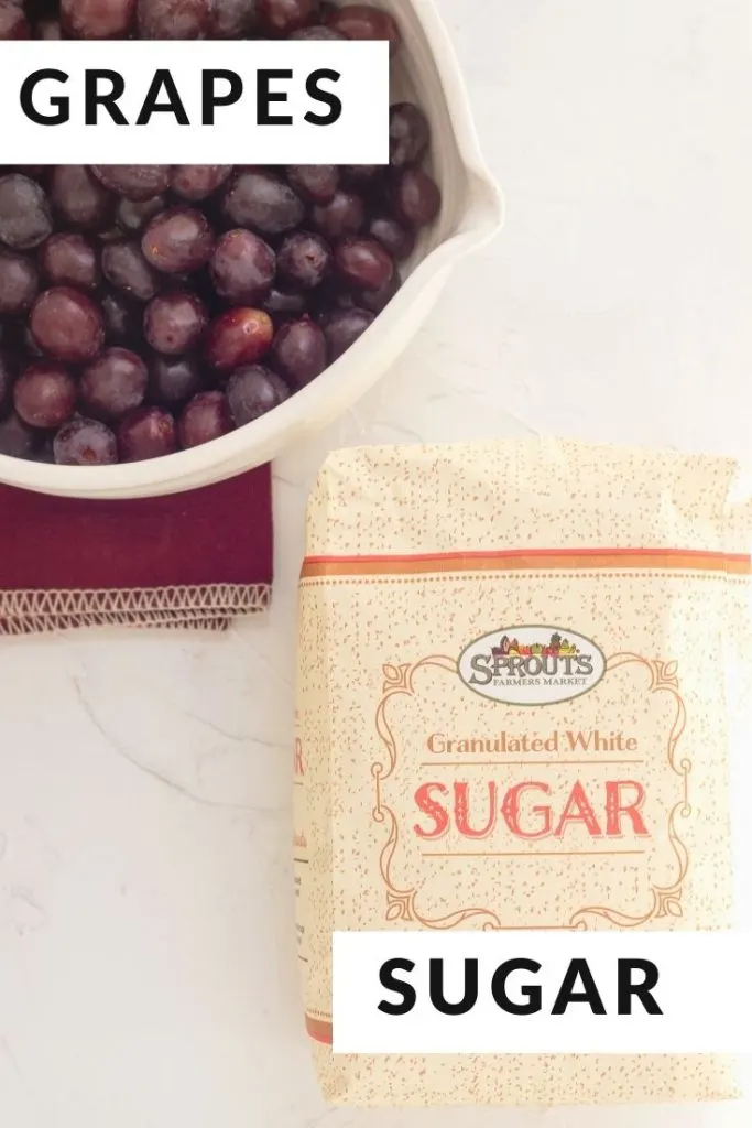 Gum Drop grapes in a white bowl and a bag of granulated sugar on a white surface