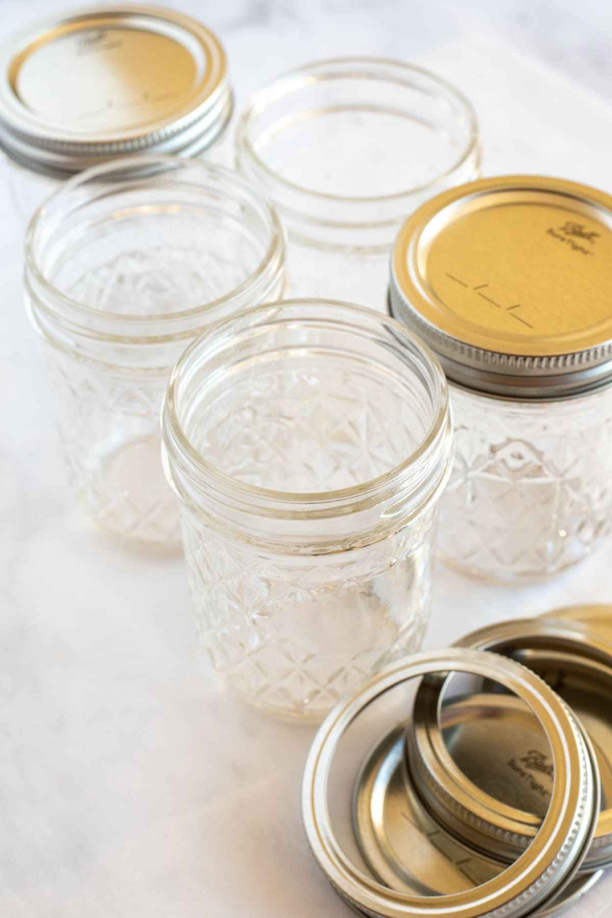 Five glass mason jars with lids and rims on white surface