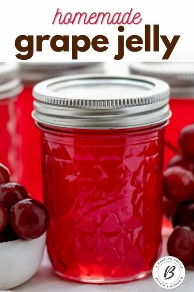 Single jar of grape jelly with silver lid and other jars in background with fresh grapes.